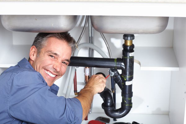 A plumber smiling while working on a sink.