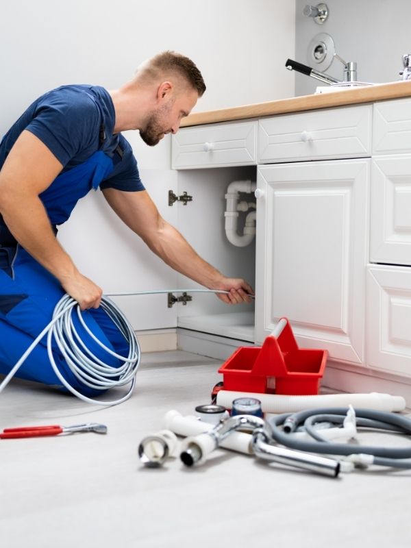 A plumber is removing soap scum clogging the kitchen pipes.