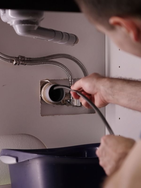 A plumber is cleaning out pipes in a kitchen.